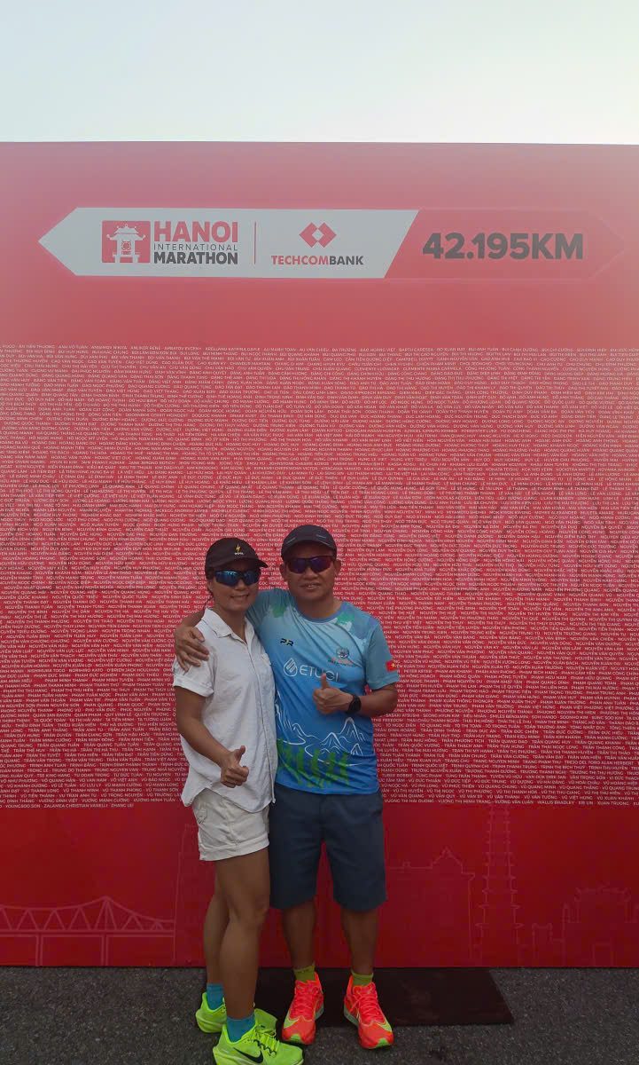 Lịch tập chạy bộ 8 tuần — vợ chồng tác giả trước backdrop 42.195KM
